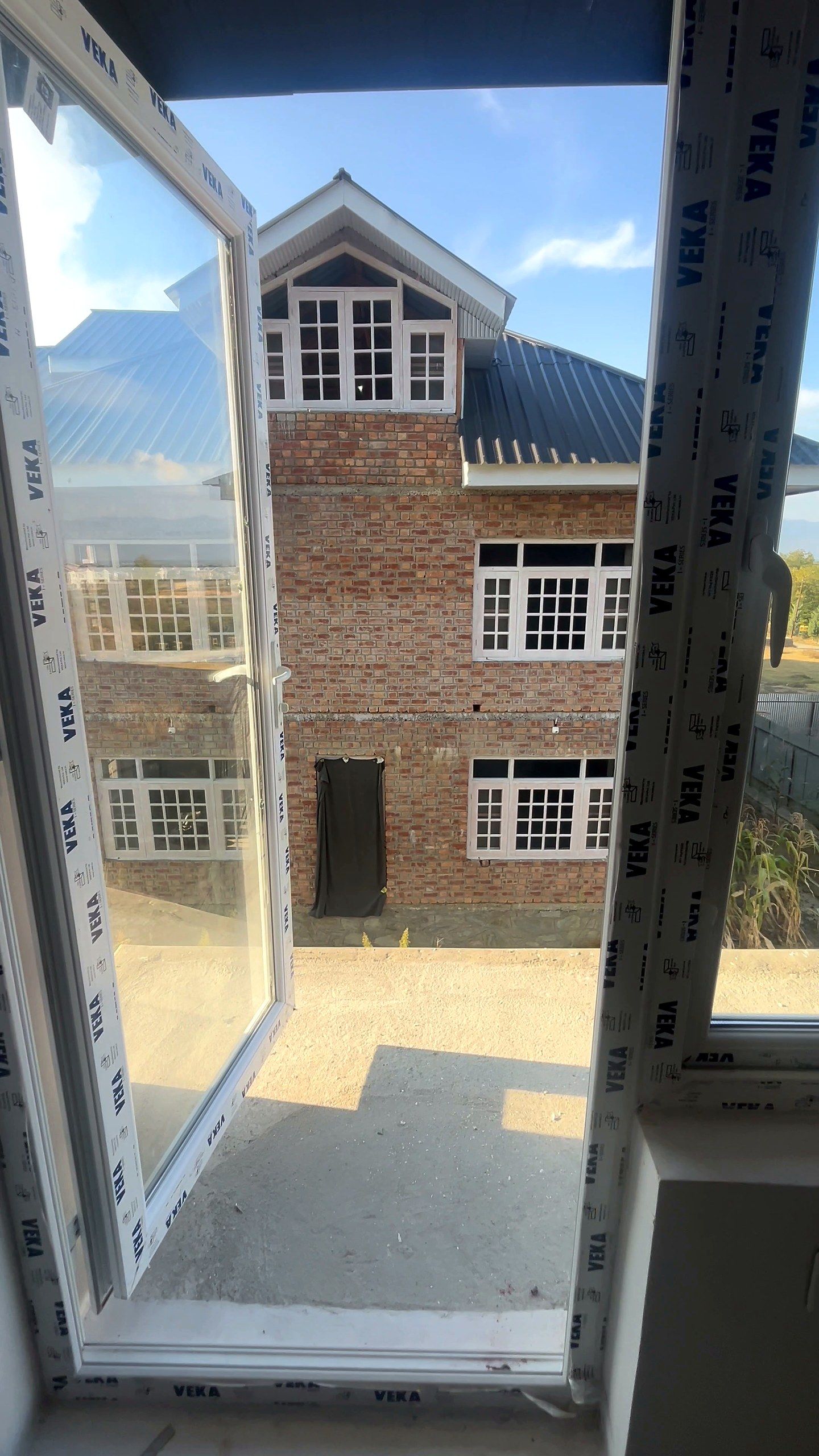 Open uPVC casement sash on a new Kashmir house, looking out at a brick house next door