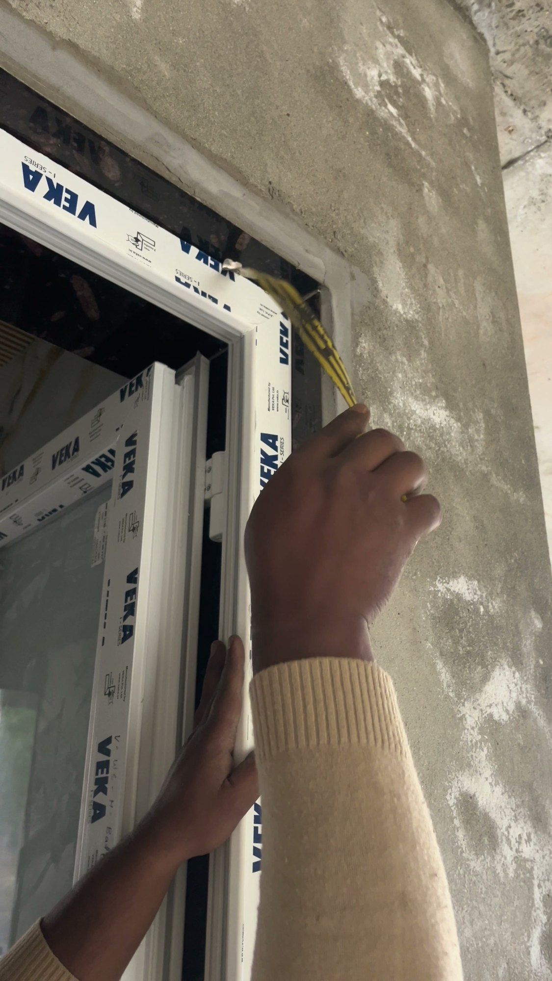Fitter checking a VEKA frame in the opening with a tape